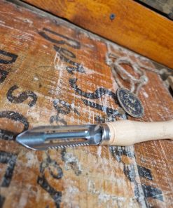 A wooden potato and vegetable peeler with a stainless steel blade. This peeler has a serrated edge for decorating root vegetables and a pointed end for poking potatoes